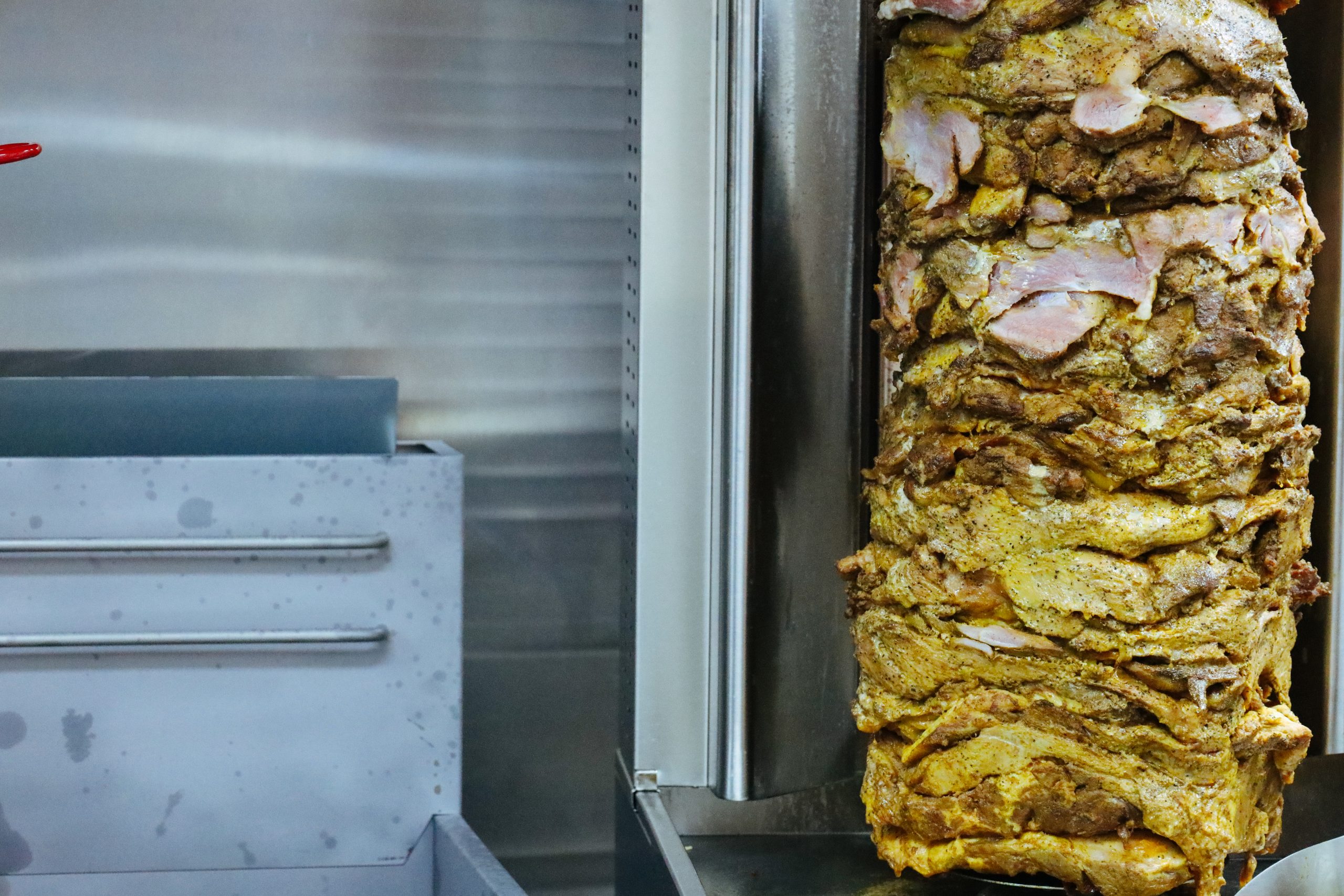 Close-up of seasoned meat stacked vertically on a rotisserie spit in a kitchen, warm yellow and brown tones