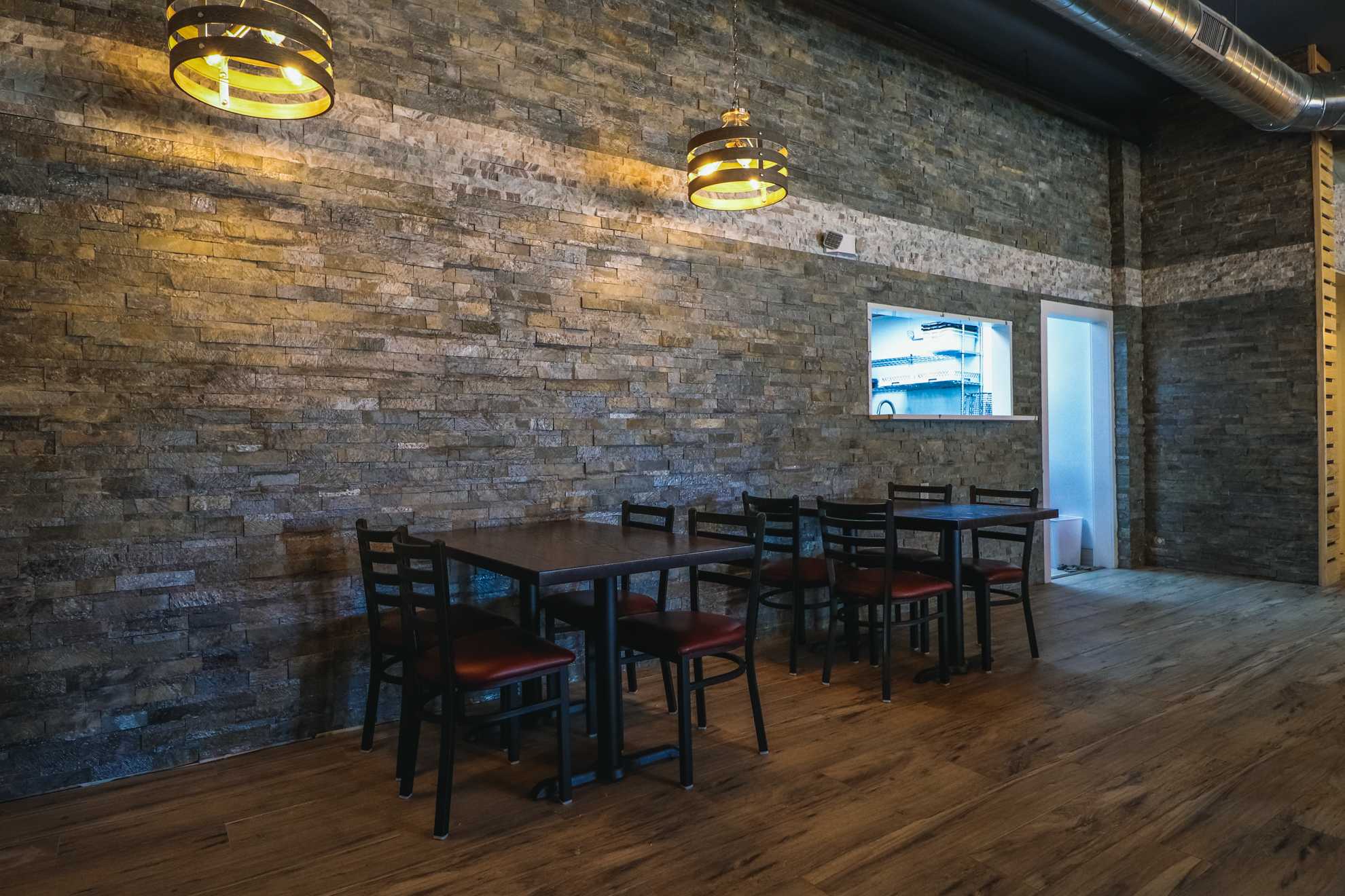 Warm restaurant dining area with a stone accent wall, wooden tables, and black chairs with red cushions under soft pendant lighting